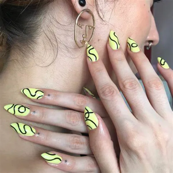 Uñas geométricas en amarillo pastel con líneas onduladas en negro